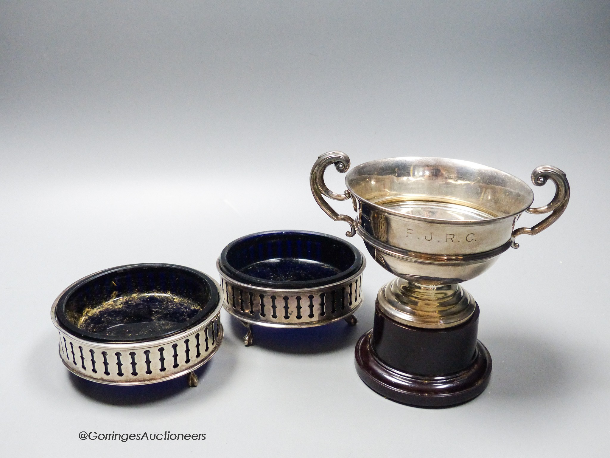 A pair of George V pieced silver small circular dishes with blue glass liners, 10cm and a silver trophy cup on stand, 6.5oz.